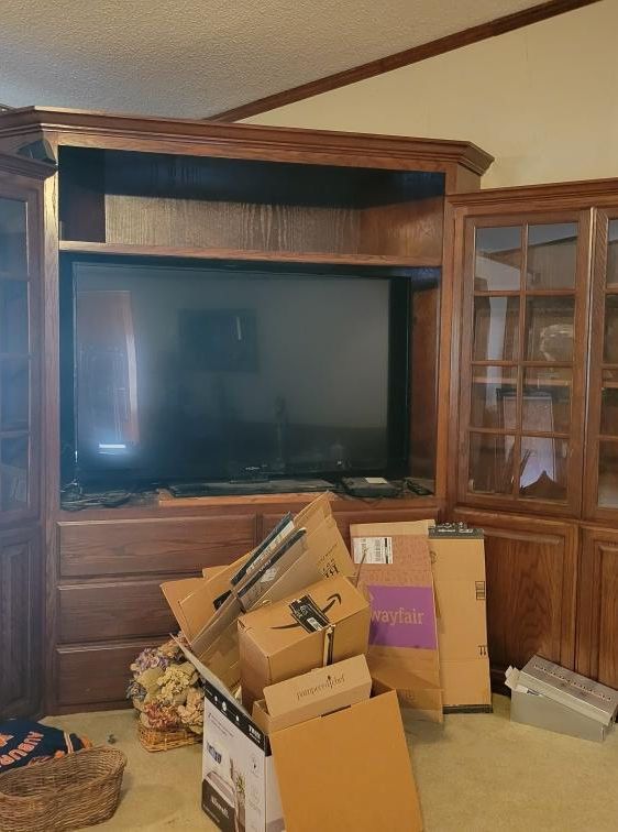 Wooden entertainment center with TV, bookcase, and cardboard boxes.