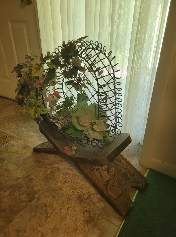 A metal and floral sculpture on a wooden stand sits in front of a window.
