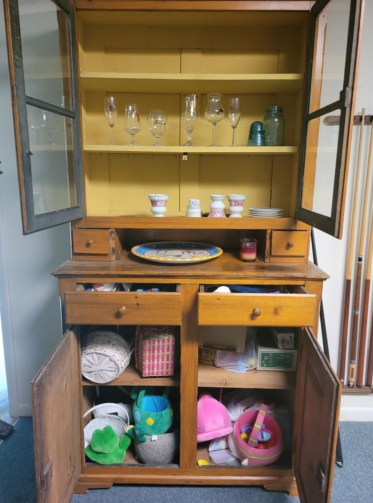 Wooden cabinet with glass-doored upper shelves and lower storage, filled with glasses, decor, and various items.