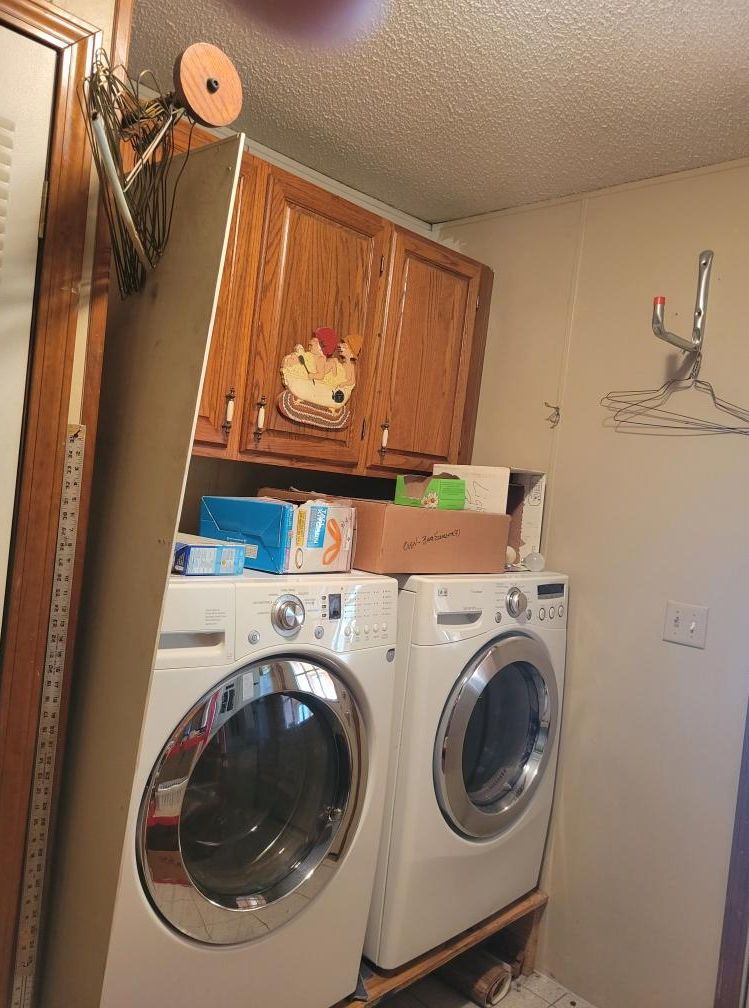 Laundry room with white washer and dryer, upper wood cabinets, and items stacked on top of machines.
