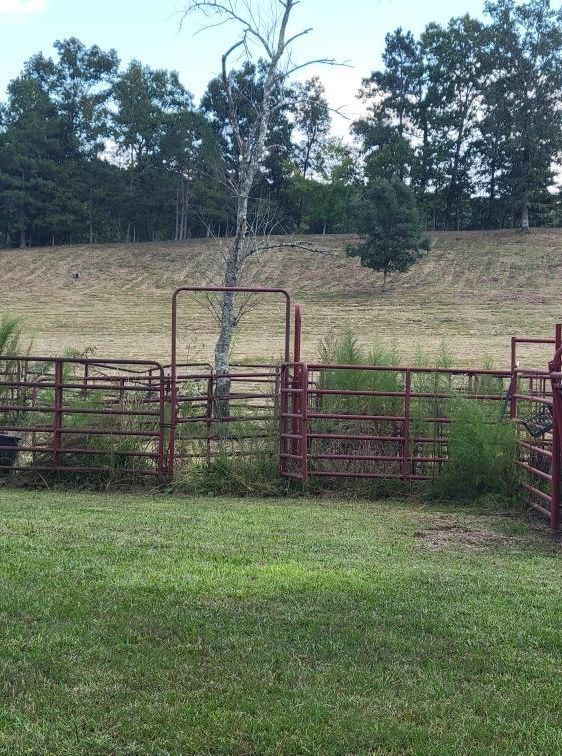 Red metal gates and fence in a grassy area with a hill and trees in the background.
