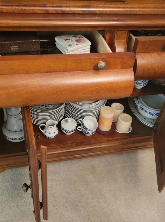 Wooden cabinet with open drawers, displaying china dishes and serving pieces.
