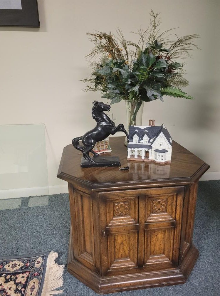 A wooden side table with a horse statue, a house figurine, and a floral arrangement.