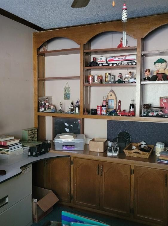 Wooden built-in shelving unit filled with collectibles, desk with clutter, in a room.