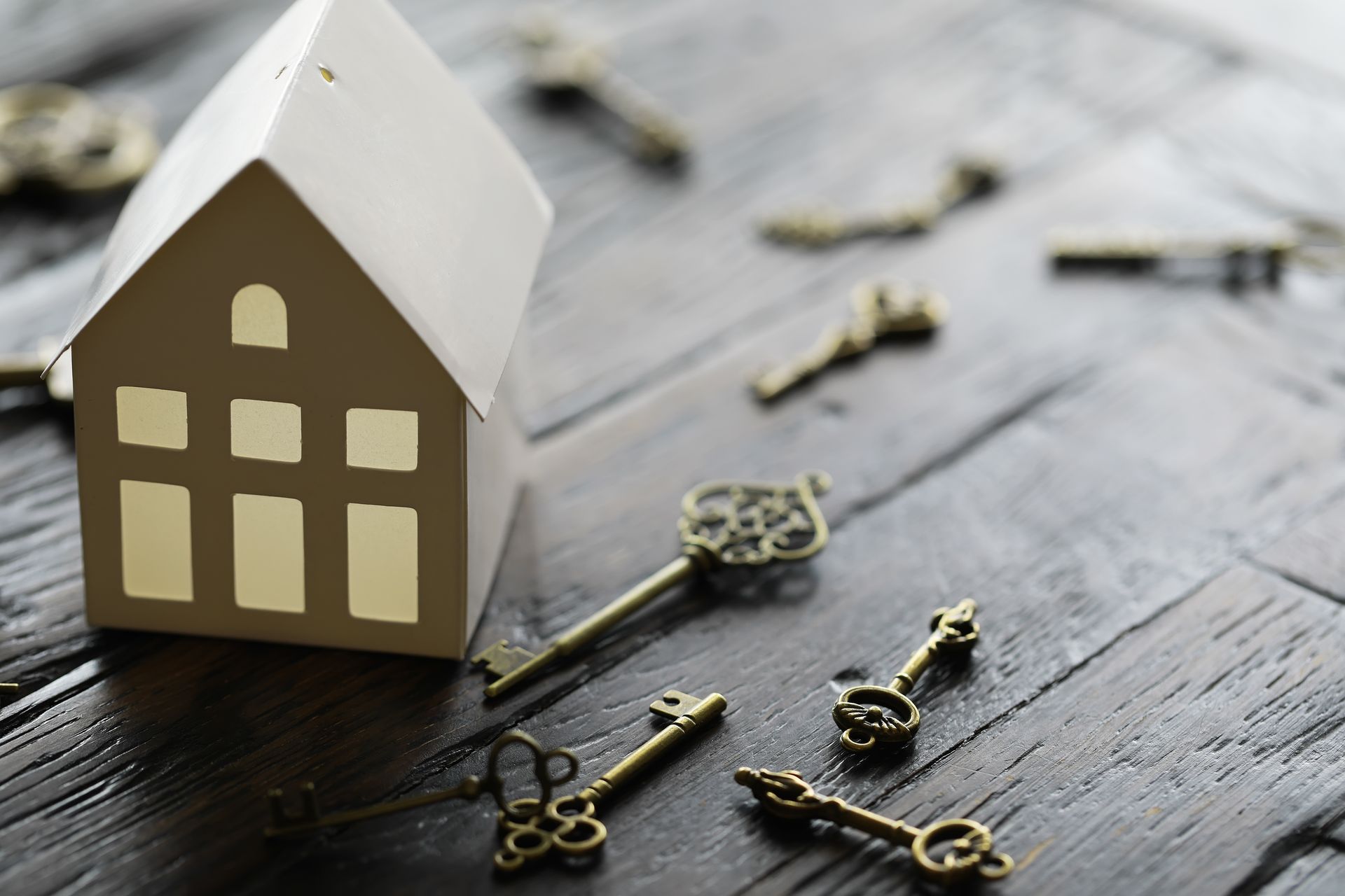 White paper house model with several antique keys on a dark wood surface. White paper house model with several antique keys on a dark wood surface.