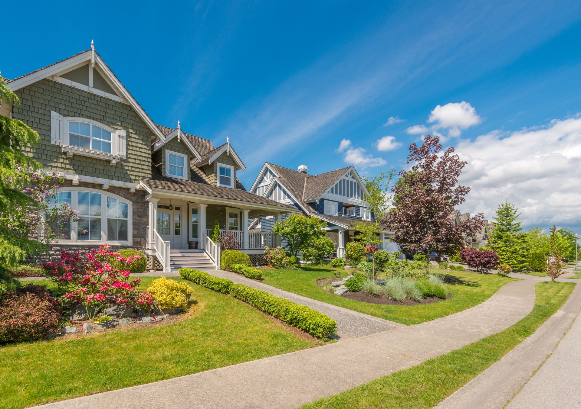 Houses with green lawns and colorful landscaping on a sunny day.