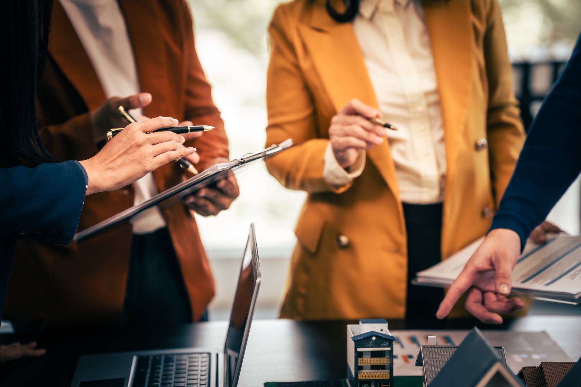 People in business attire reviewing documents and models around a table.