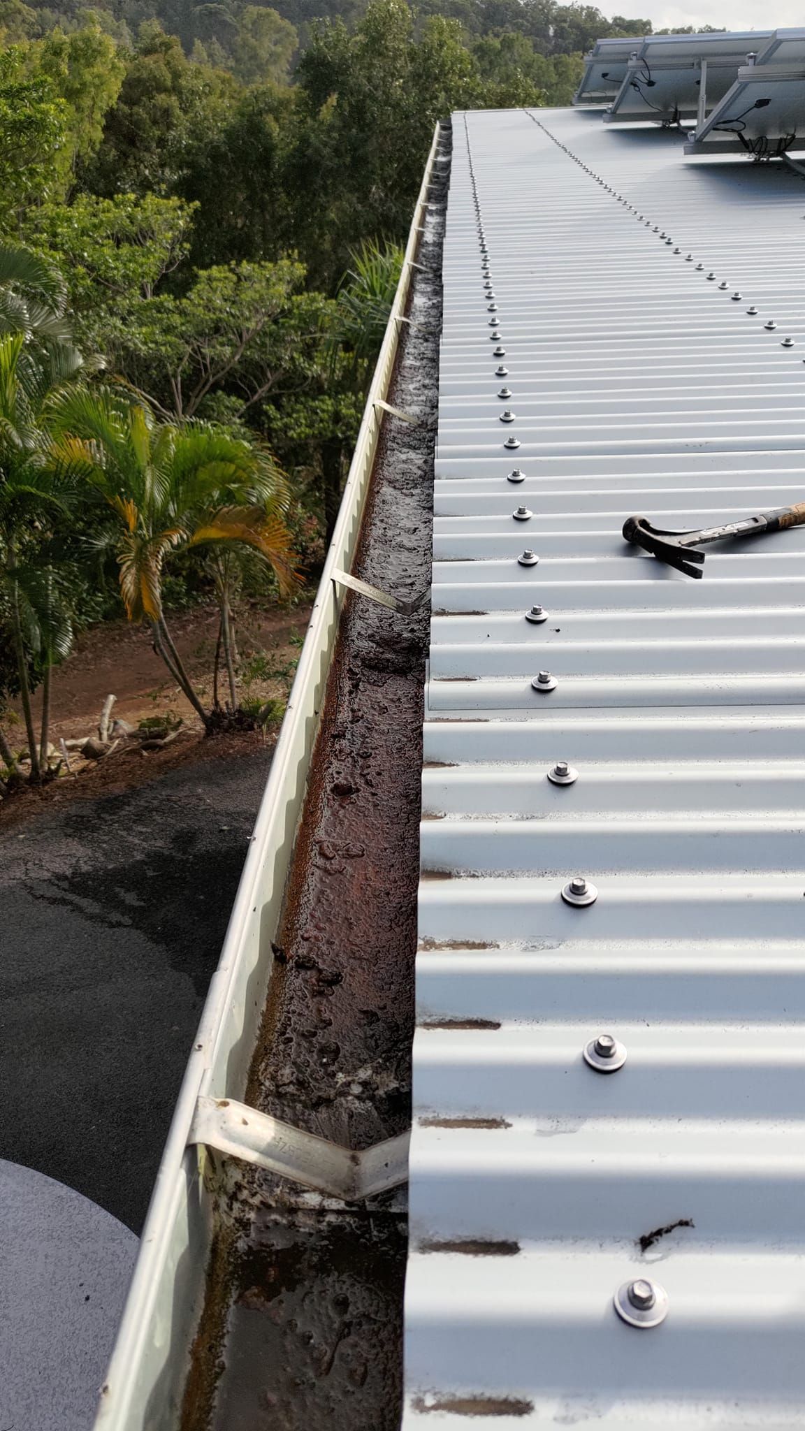 A Metal Roof Edge Next to a Gutter Filled With Debris — Rhettro Roofing Industry in Taroomball, QLD