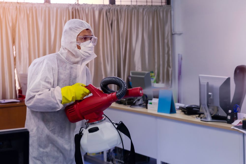 A Man in A Protective Suit Is Disinfecting an Office with A Sprayer — Port O' Call Cleaning In Bowen, QLD