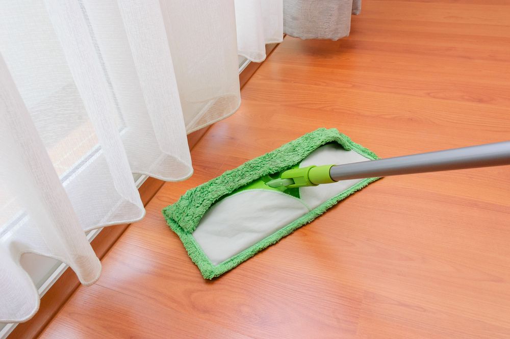 A Flat Green and White Mop Cleaning a Wooden Floor Near a Window — Port O' Call Cleaning In Cannon Valley, QLD