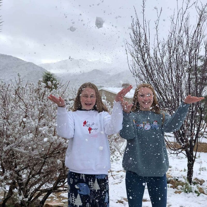Two young girls are throwing snow in the air.