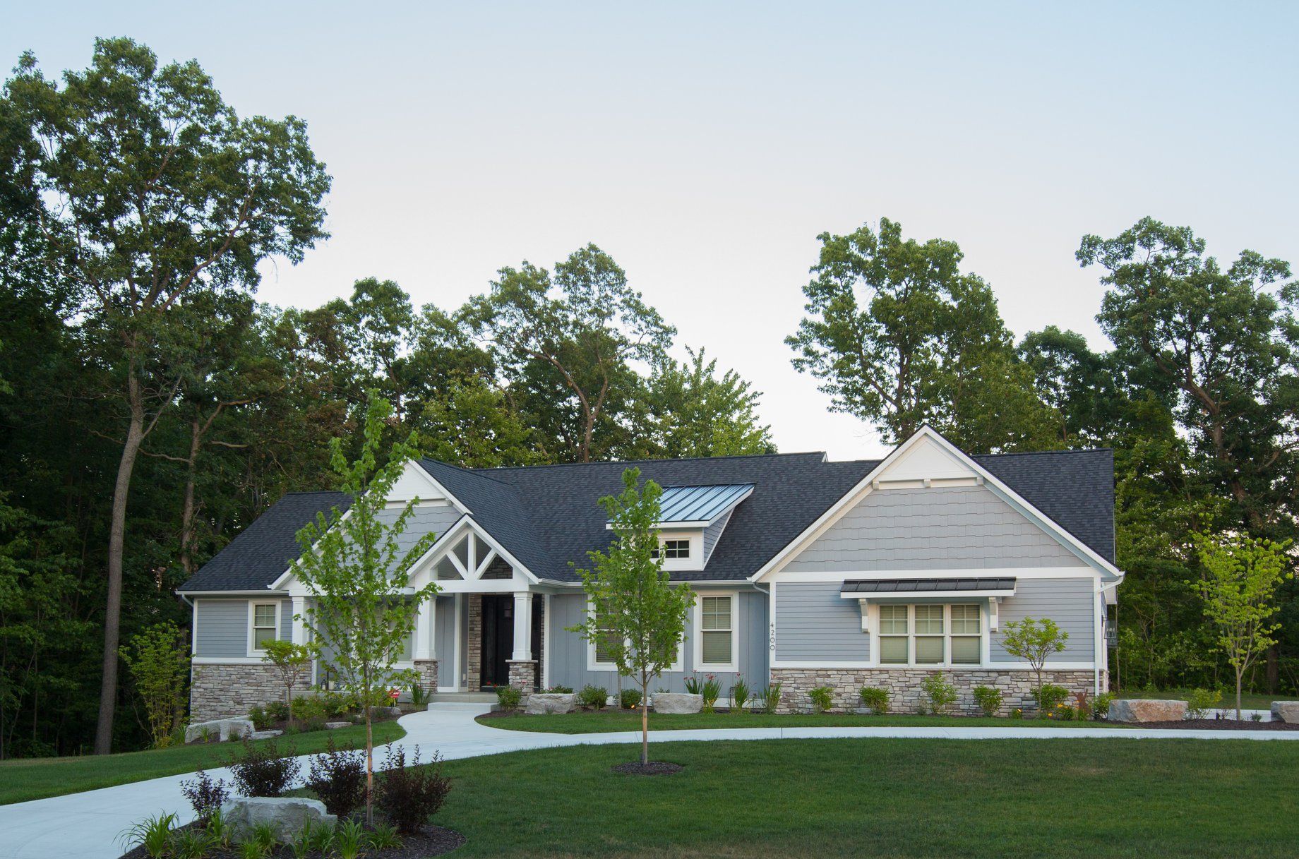 A gray house with a black roof is surrounded by trees
