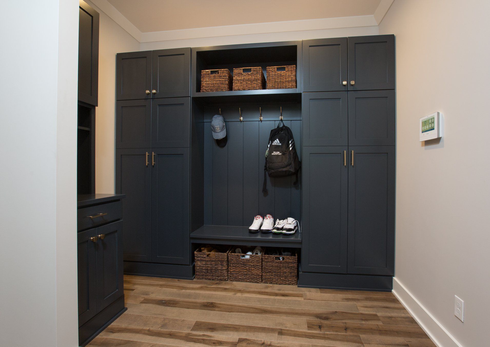 A mud room with lots of cabinets , baskets , and a bench.