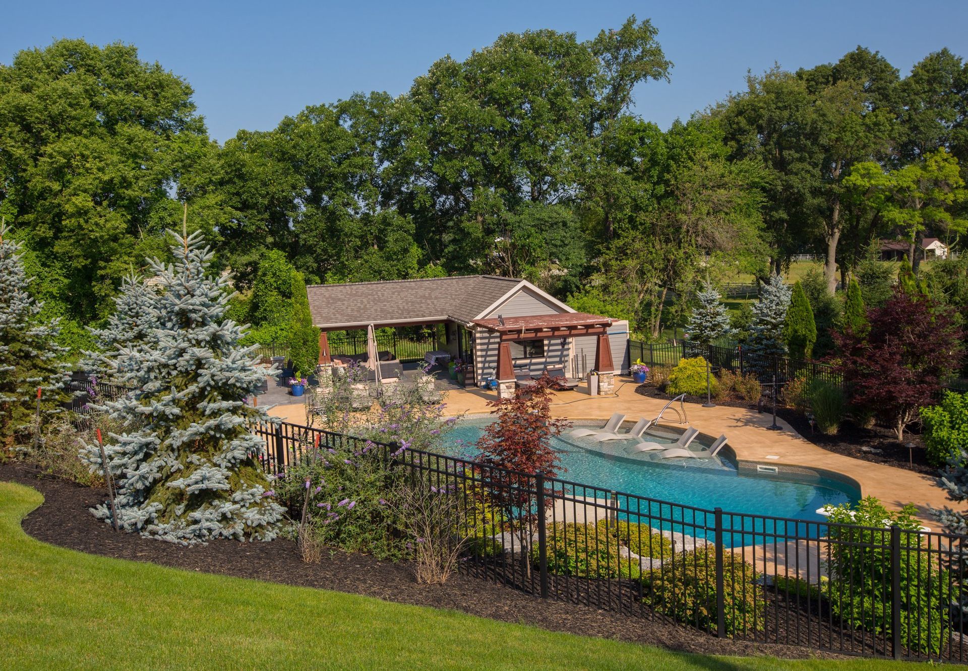 A large swimming pool is surrounded by trees and a fence
