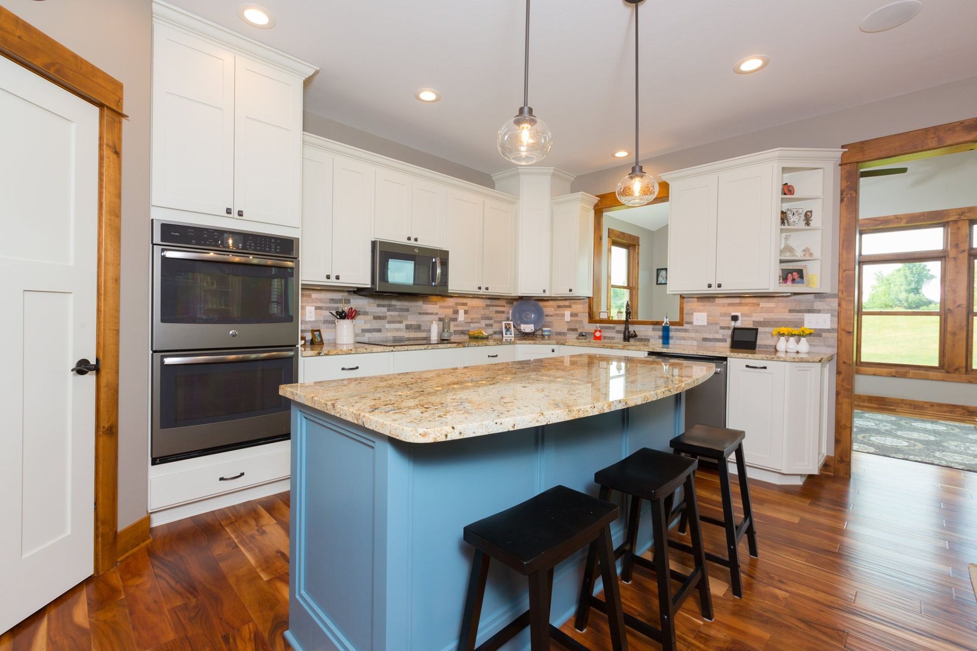 A kitchen with a blue island , white cabinets , granite counter tops and stools.