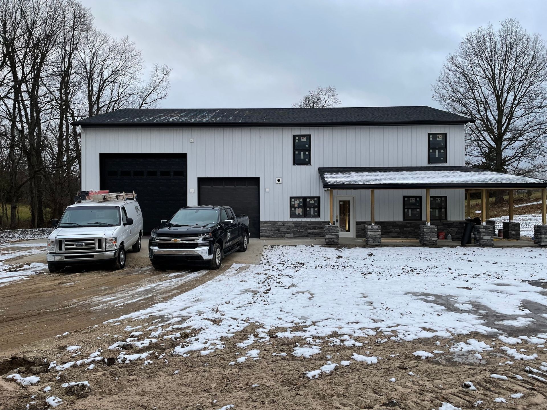 Two trucks are parked in front of a house in the snow.