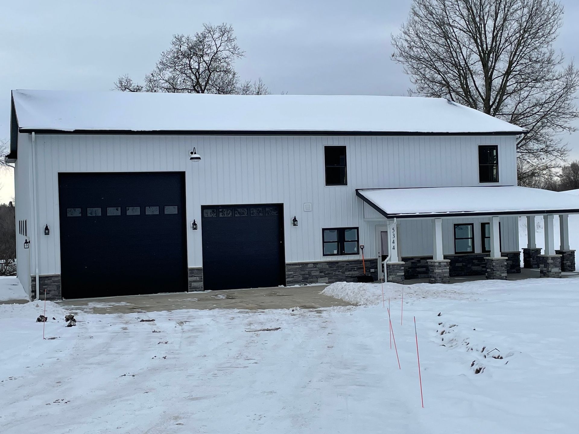 A white house with black garage doors and a porch in the snow.