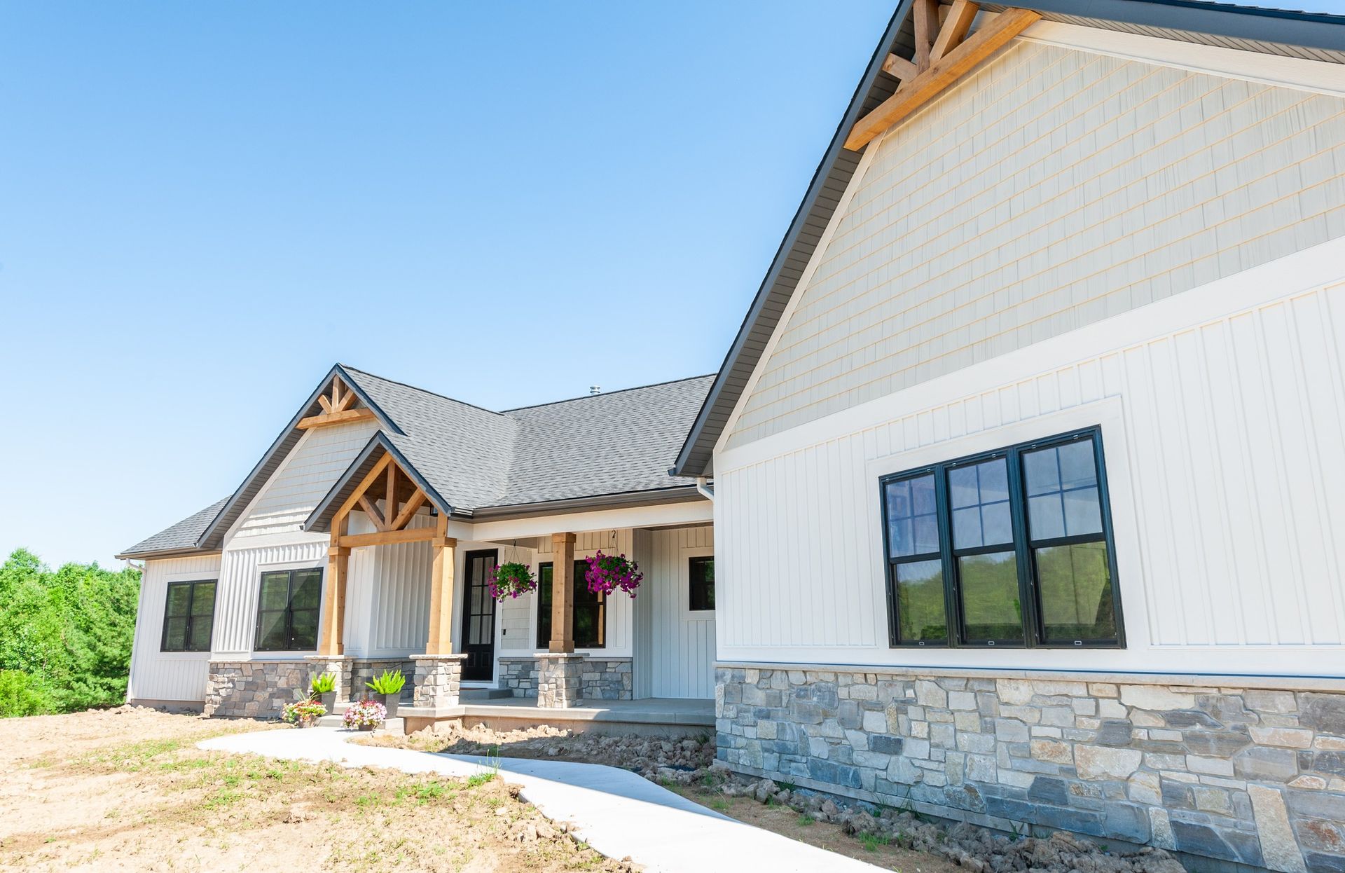 A large white house with a black roof is sitting on top of a dirt field.