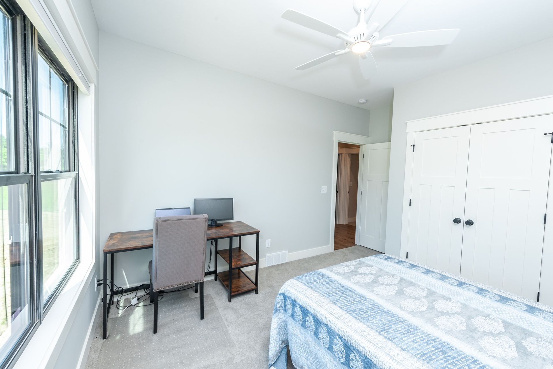 A bedroom with a bed , desk , chair and ceiling fan.