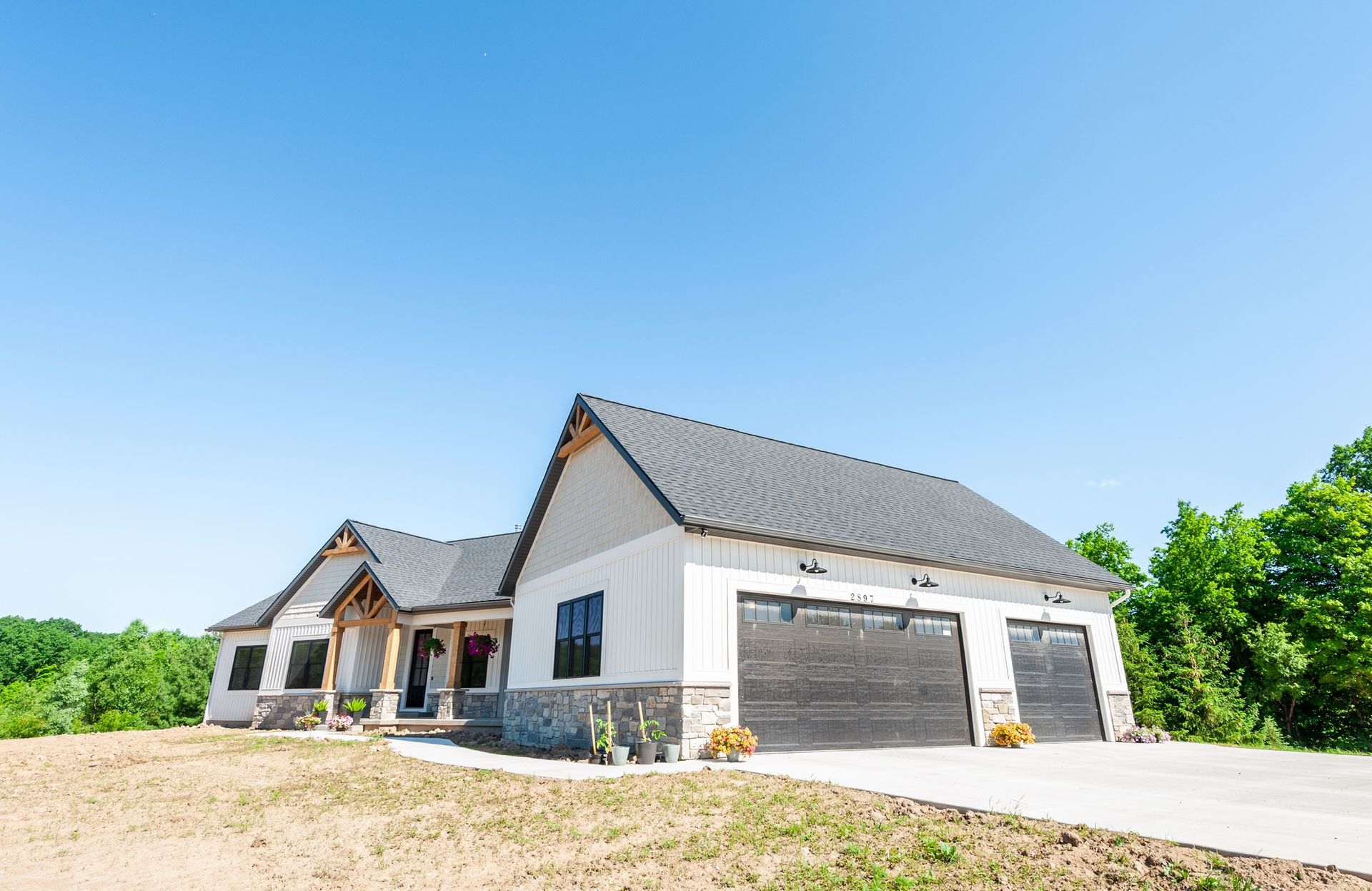 A large white house with a black roof is sitting on top of a dirt hill.
