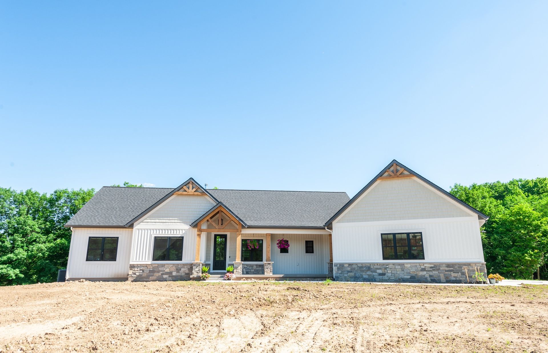 A white house with a gray roof is sitting on top of a dirt field.