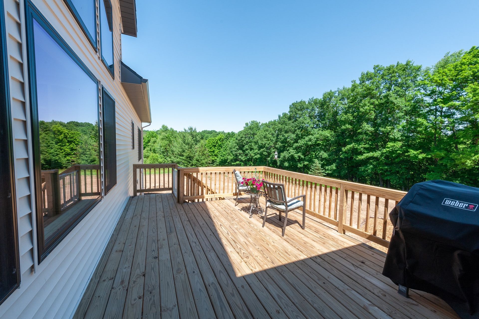 A large wooden deck with a grill and chairs on it