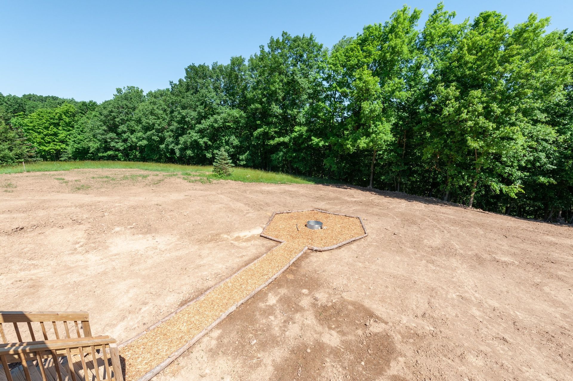 A dirt field with trees in the background and a bench in the foreground