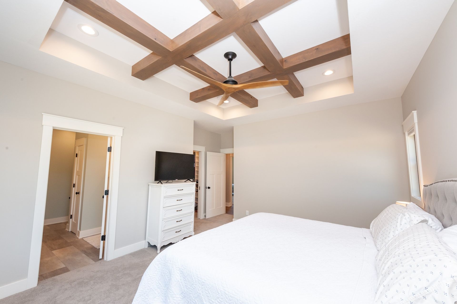 A bedroom with a bed , dresser , television and ceiling fan.