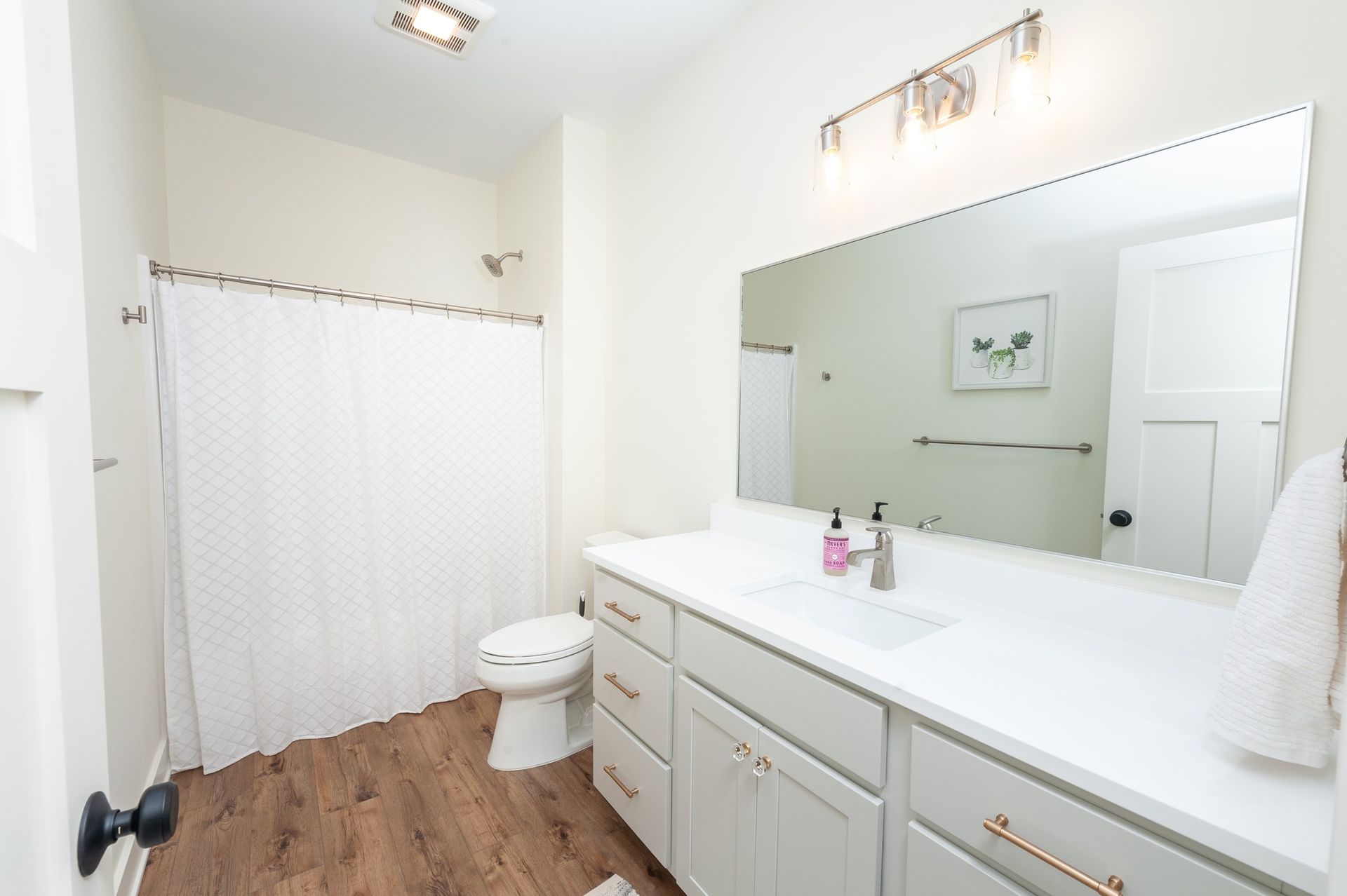 A bathroom with a toilet , sink , mirror and shower curtain.