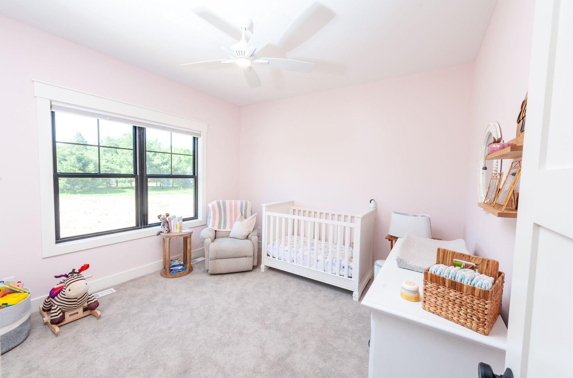 A nursery with a crib , chair , dresser and two windows.