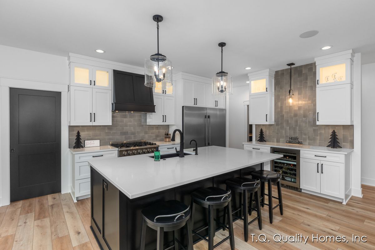 A kitchen with white cabinets and black stools and a large island.