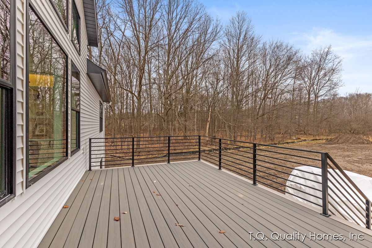 There is a large deck with a railing and trees in the background.