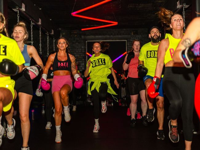 a group of people wearing boxing gloves are running in a gym .