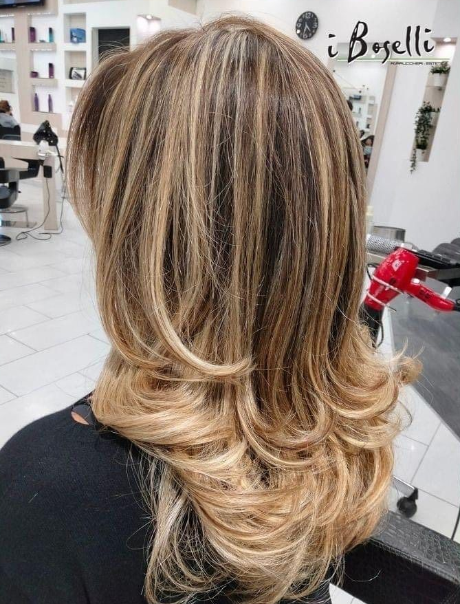 Edificio a tre piani con facciata beige e grigia, posti a sedere nel patio, grande albero, ambientazione montuosa.