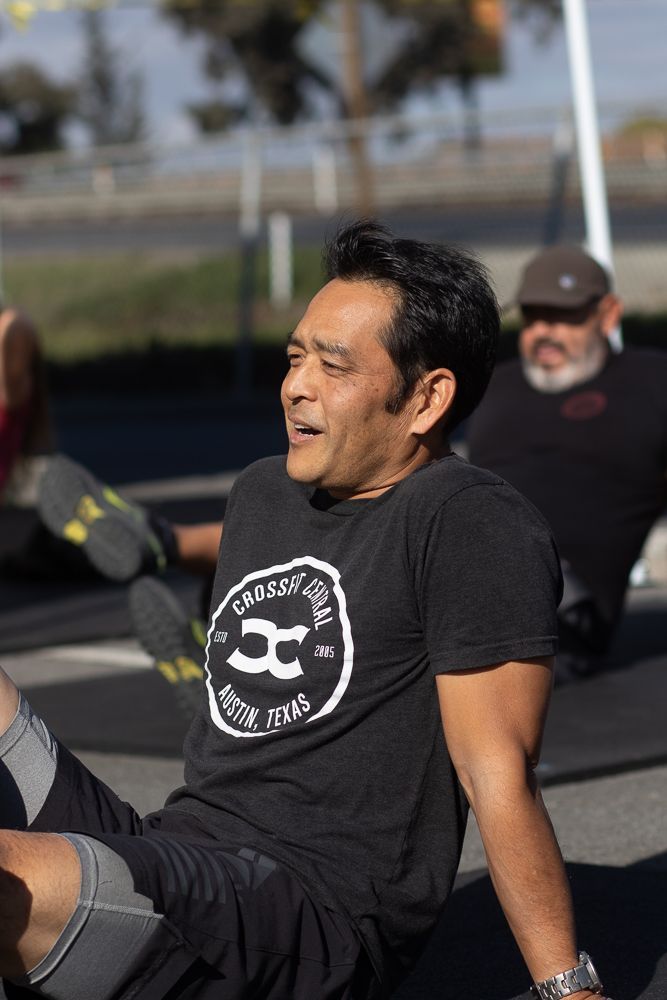 A man in a black t-shirt is stretching his legs.