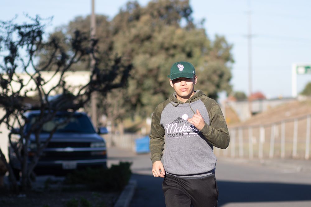 A man is running down a street wearing a hat and a sweatshirt.