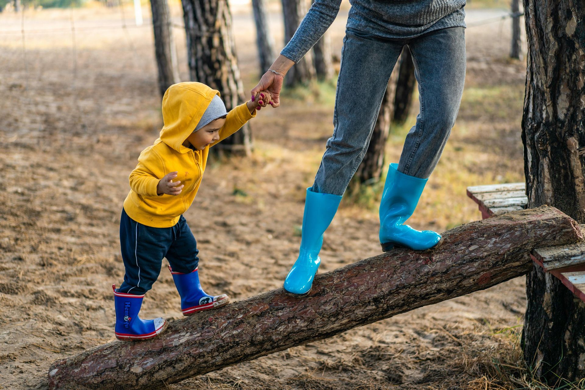 A woman is helping a little boy balance on a log.