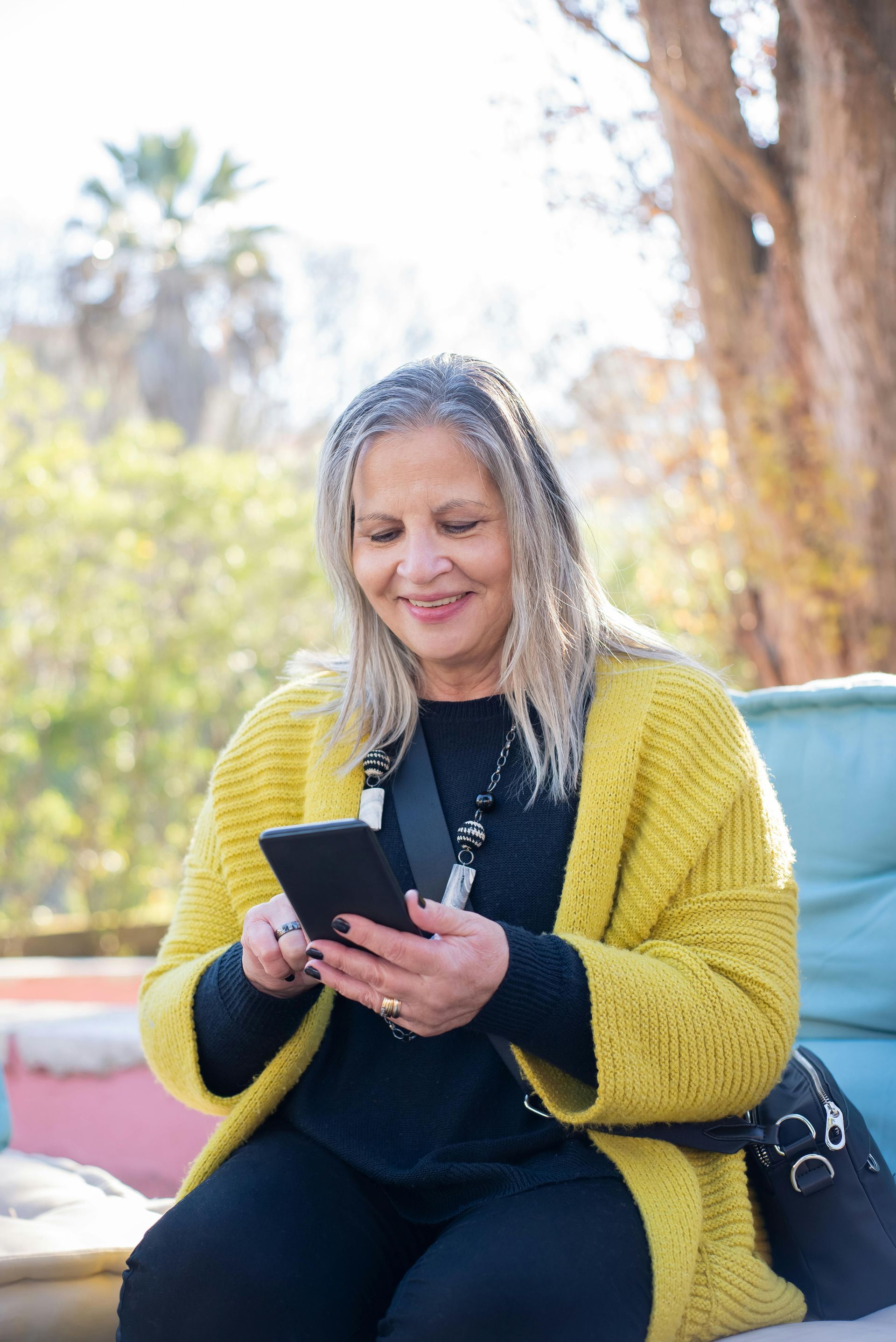 A woman in a yellow sweater is sitting on a couch looking at her cell phone.