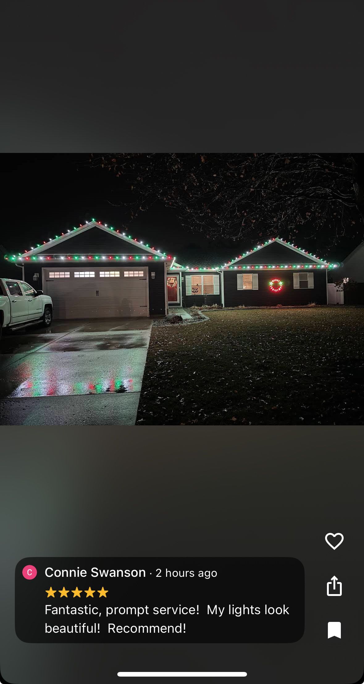 House at night with Christmas lights on the roof and a wreath. Snow falling.