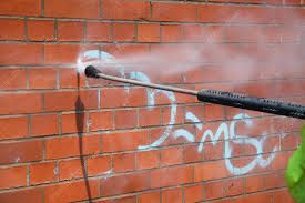 Pressure-washing graffiti off a red brick wall
