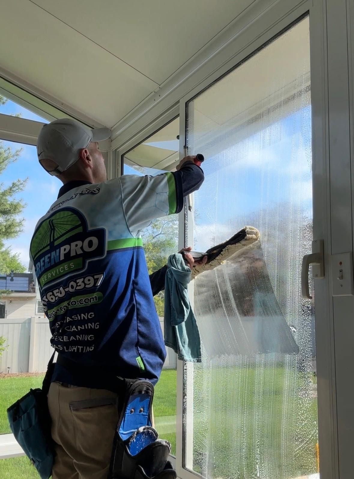 Worker cleaning a glass door on a sunlit porch with a squeegee