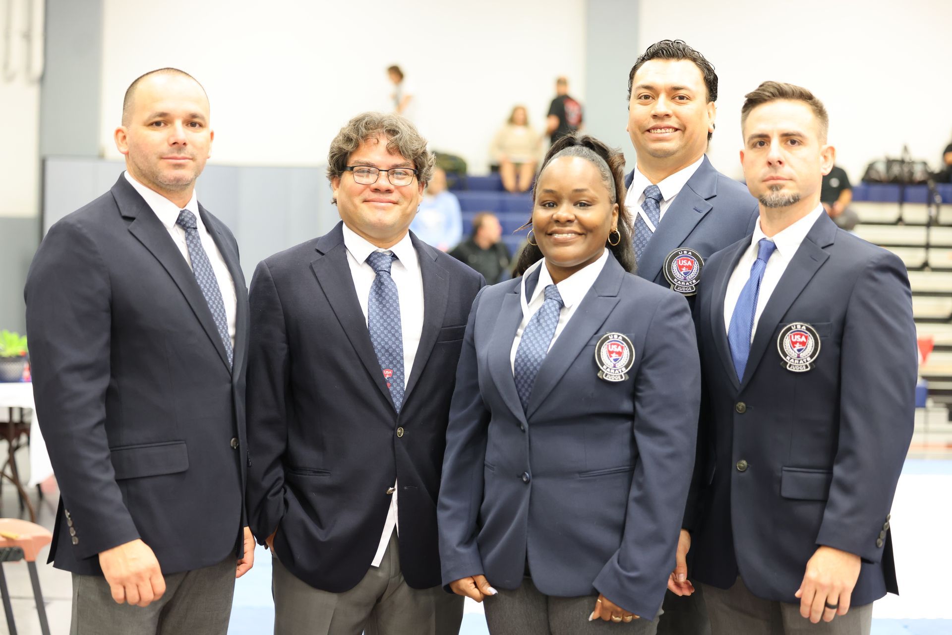 Five referees in blue blazers, posing for a photo in a gymnasium.