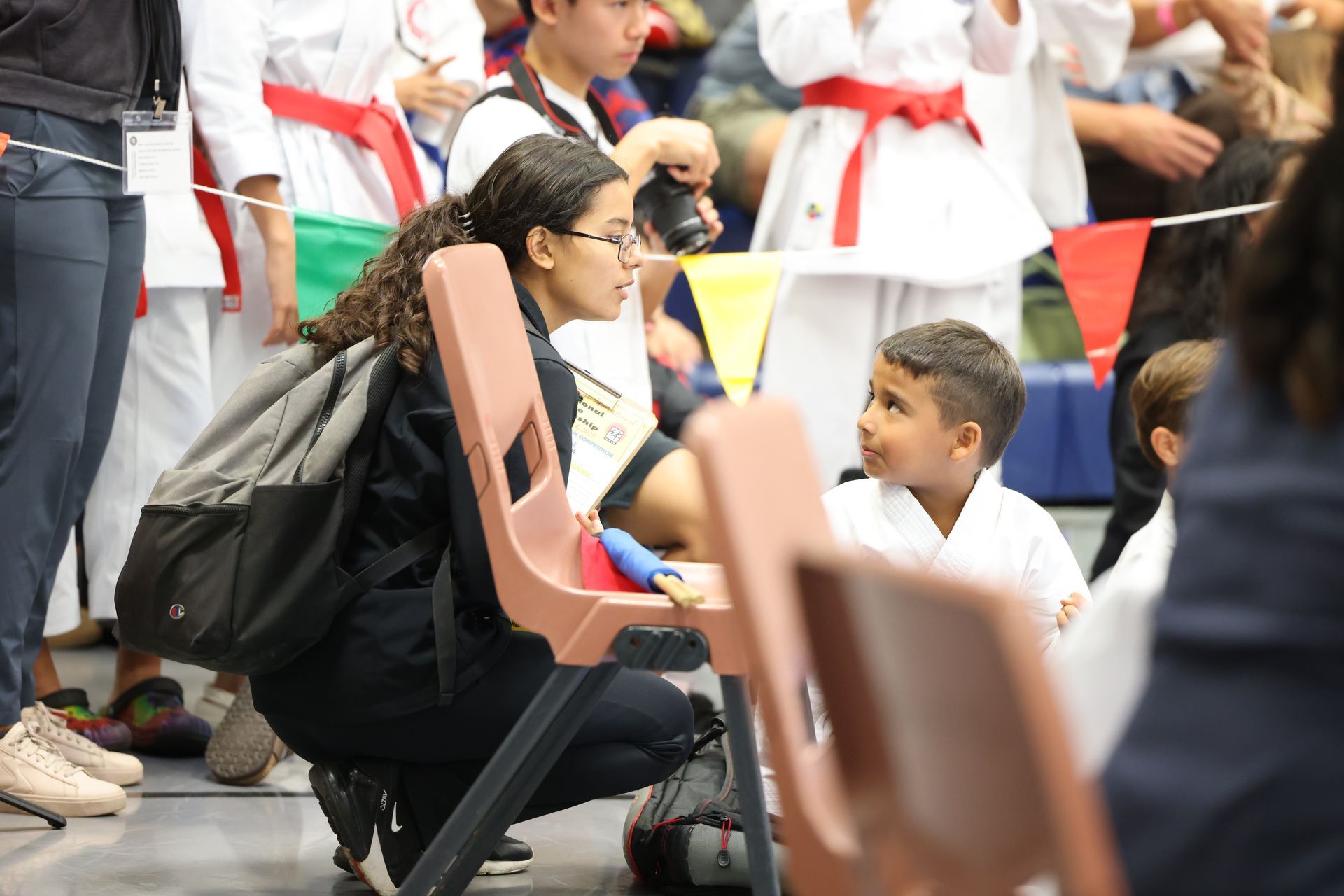 Woman in glasses talking to a young boy in a karate uniform at a competition.