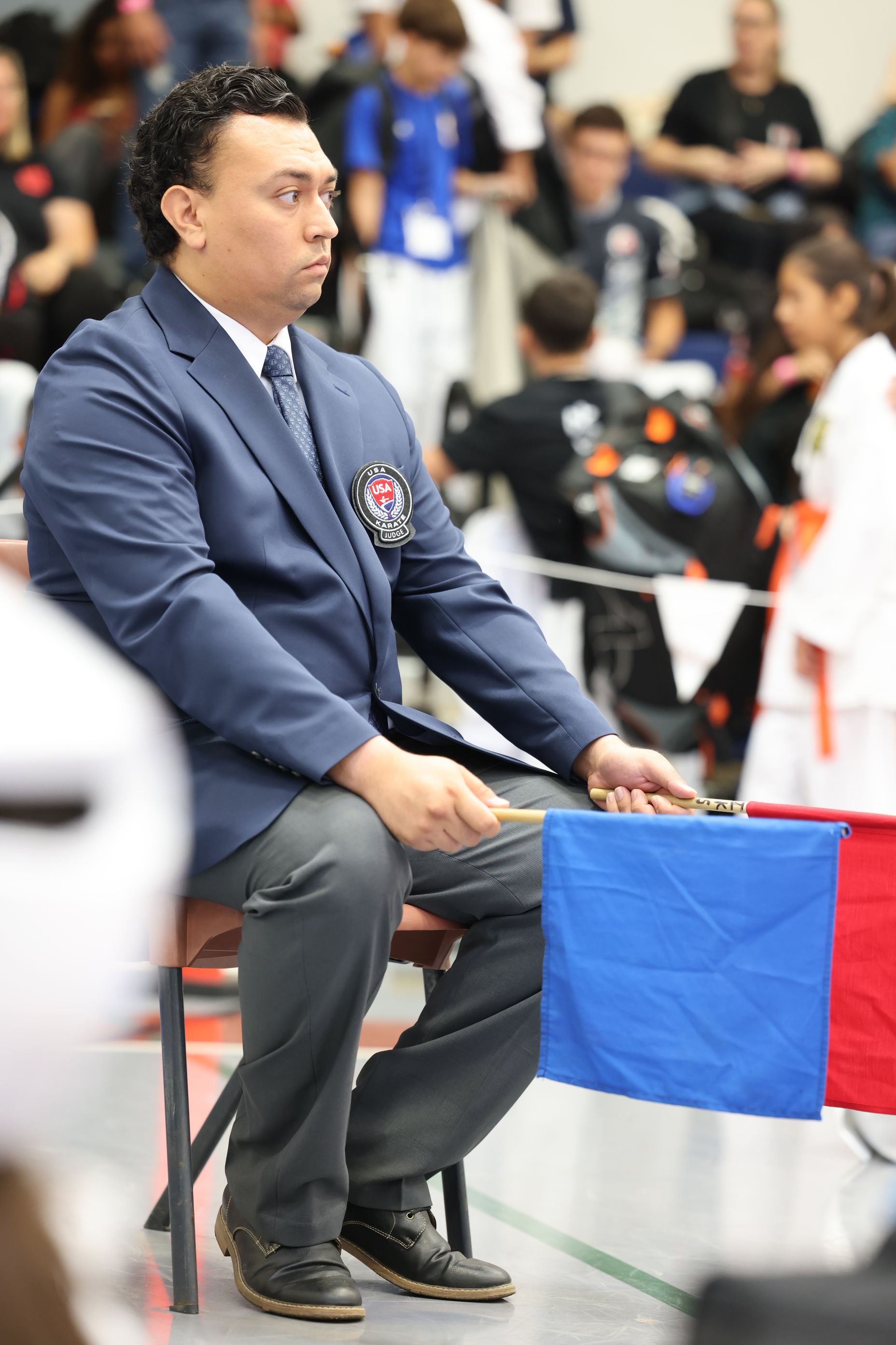 Referee at a martial arts competition, seated and holding blue flag.