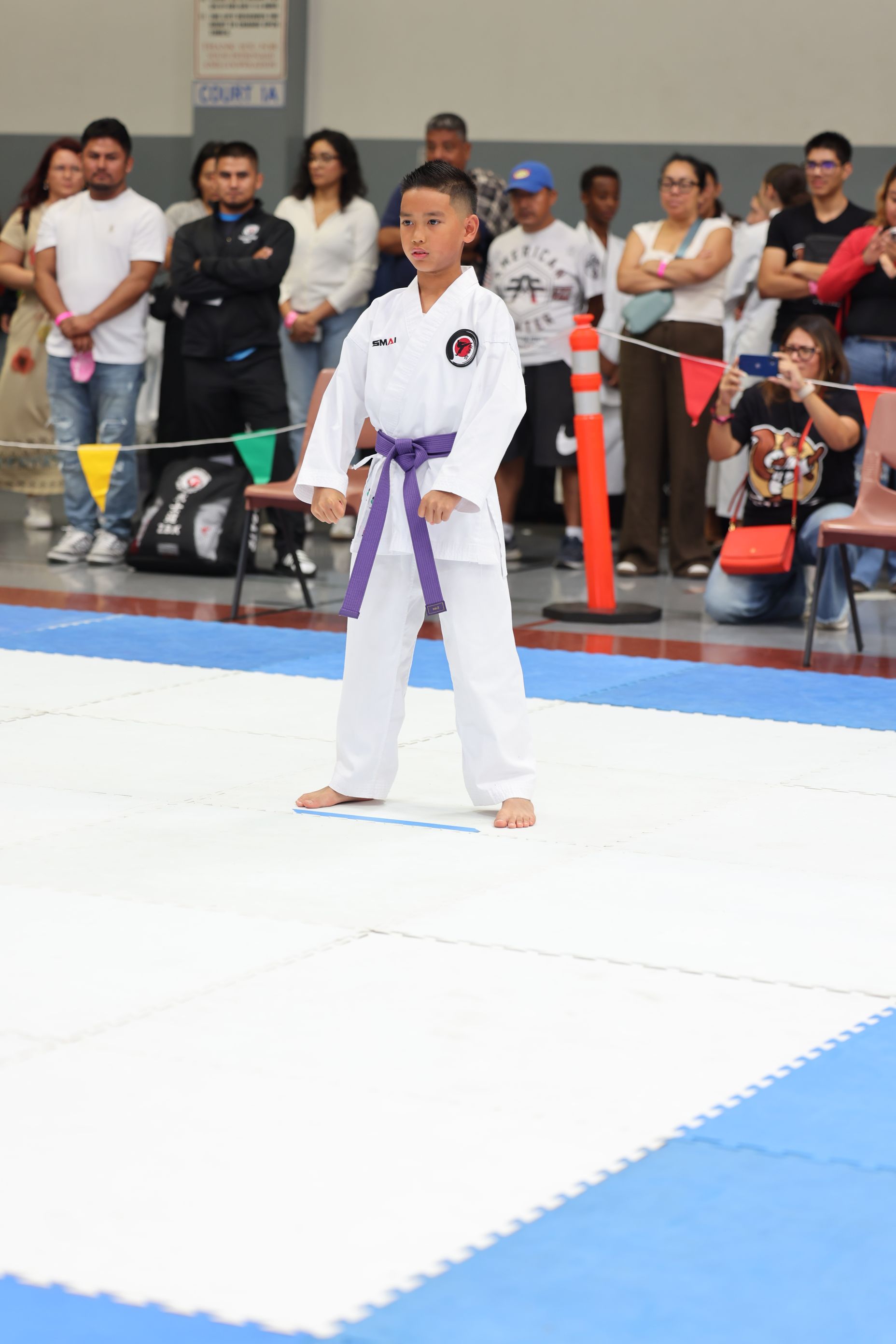 Boy in karate uniform with purple belt on a blue and white mat, performing kata.