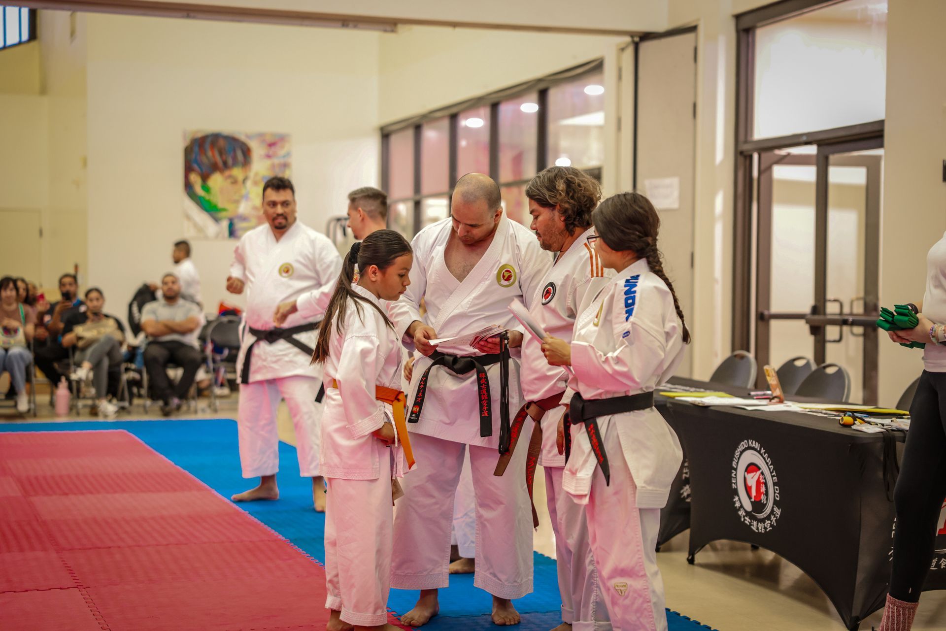 Martial arts students in white uniforms and belts receive awards from an instructor indoors.