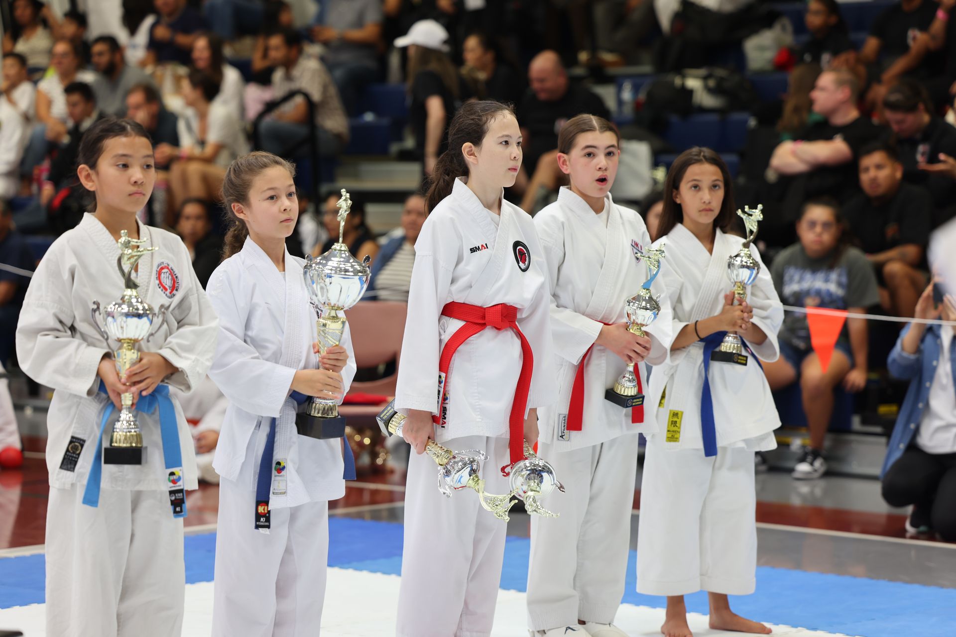 Young karate champions holding trophies on a podium, in a competition setting.