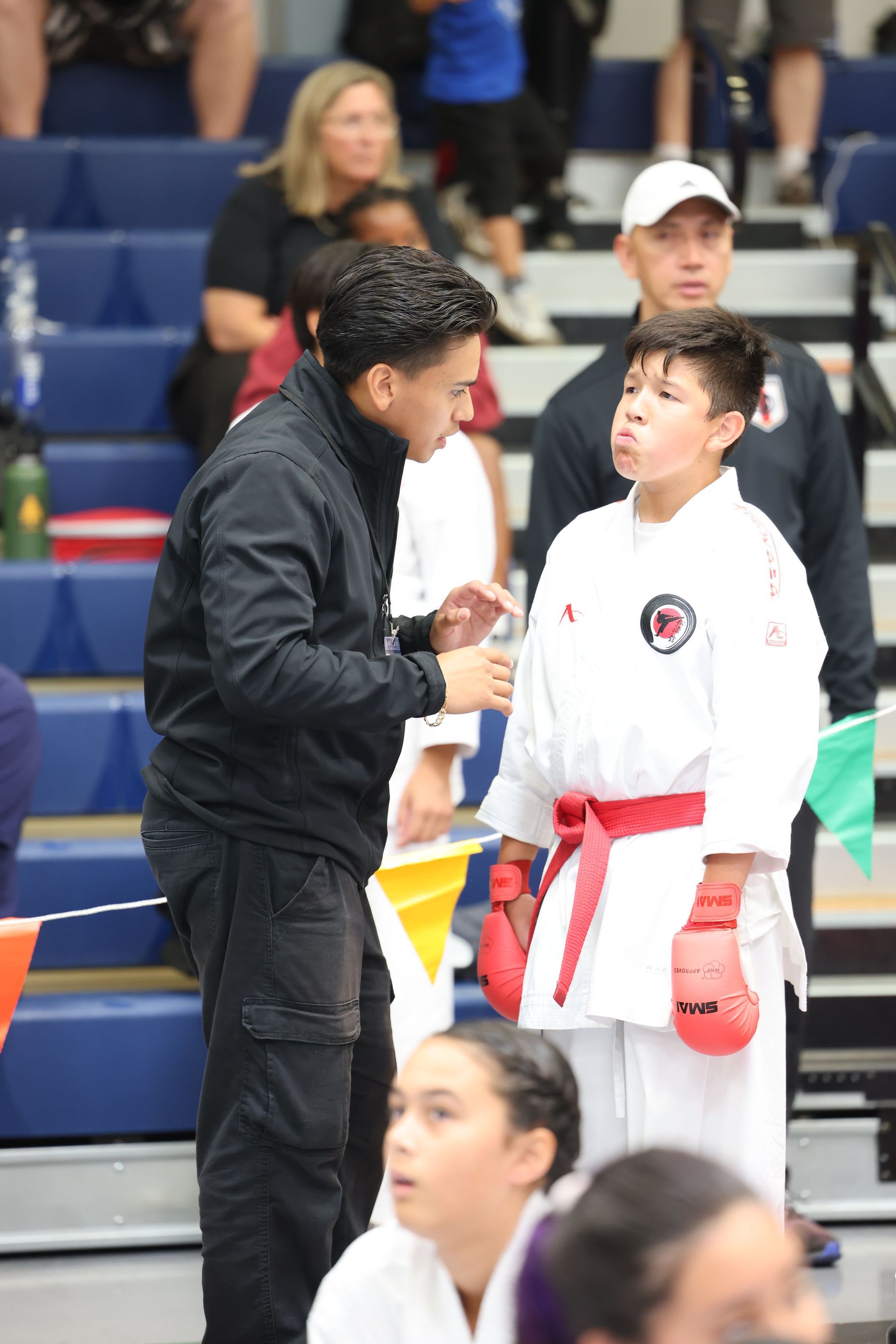 Karate coach talking to young competitor wearing a red belt at a tournament.