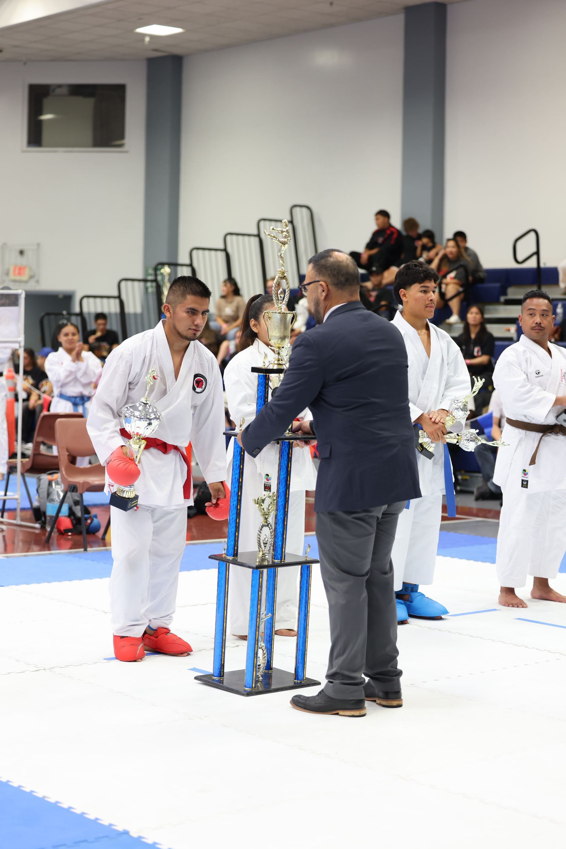 Karate tournament award ceremony; man presenting trophies to young karate competitors in white gis.