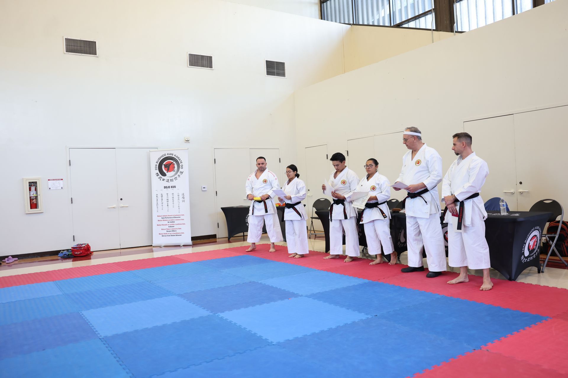 A group of people are standing on a karate mat in a gym.